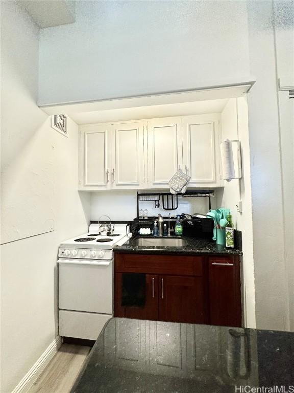 kitchen featuring white electric range, sink, white cabinets, dark stone counters, and light hardwood / wood-style floors