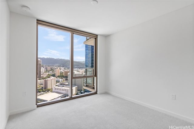 carpeted empty room with expansive windows, baseboards, a view of city, and a mountain view