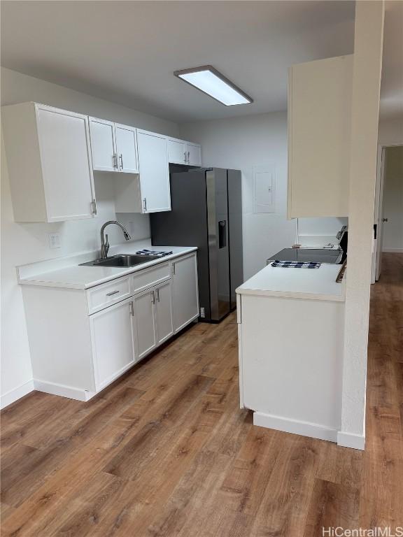 kitchen with baseboards, stainless steel fridge with ice dispenser, light countertops, light wood-style floors, and a sink