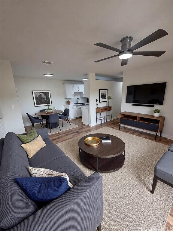 living room with light wood-type flooring, visible vents, baseboards, and a ceiling fan