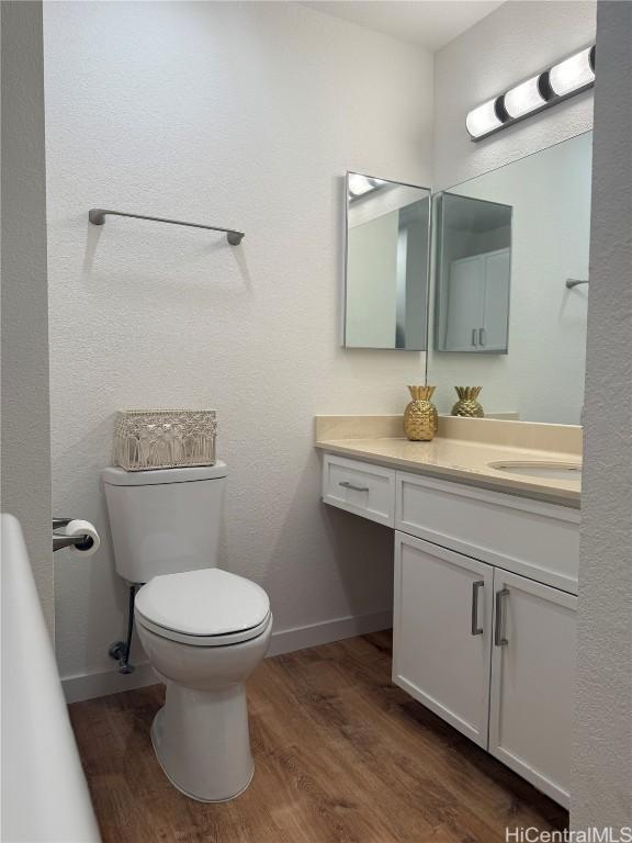 half bathroom with baseboards, vanity, toilet, and wood finished floors