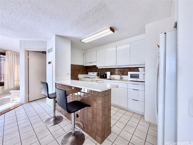 kitchen featuring sink, white appliances, backsplash, a kitchen breakfast bar, and white cabinets