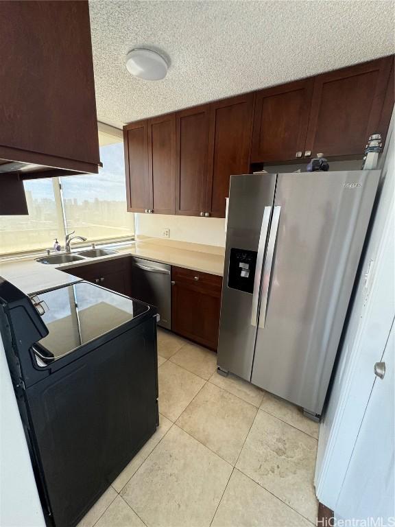 kitchen featuring a textured ceiling, appliances with stainless steel finishes, light countertops, and a sink