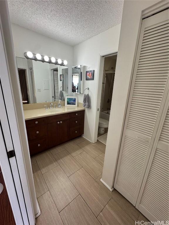 bathroom with toilet, vanity, a textured ceiling, wood finish floors, and a closet