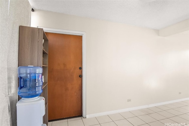 empty room featuring a textured ceiling, baseboards, and light tile patterned floors