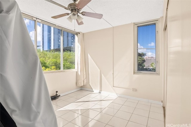 unfurnished room with a textured ceiling, light tile patterned floors, a ceiling fan, and baseboards