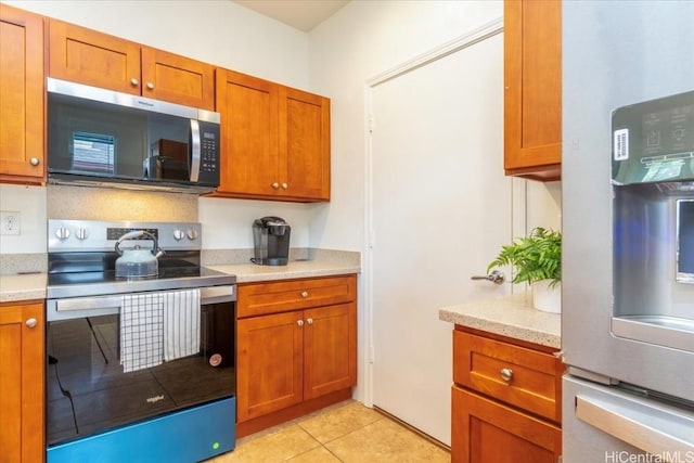 kitchen with light tile patterned floors, brown cabinets, and appliances with stainless steel finishes