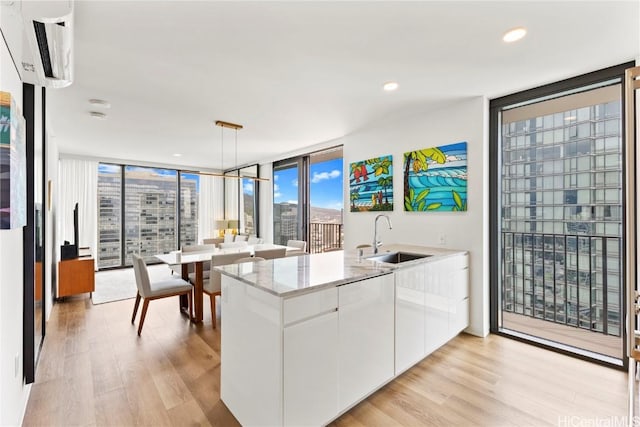 kitchen with decorative light fixtures, a city view, expansive windows, white cabinets, and a sink