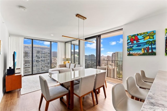 dining space featuring light wood-style flooring, a view of city, and a wall of windows