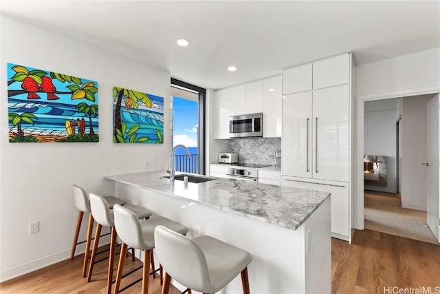 kitchen featuring stainless steel appliances, white cabinets, a sink, a peninsula, and a kitchen bar