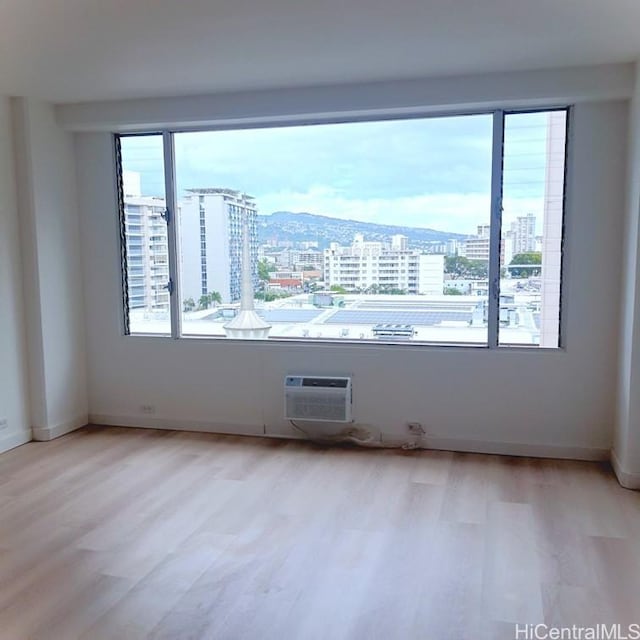 spare room featuring a wall unit AC, light wood-style flooring, a view of city, and baseboards