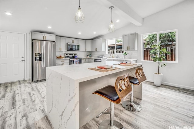 kitchen with appliances with stainless steel finishes, gray cabinetry, lofted ceiling with beams, and pendant lighting