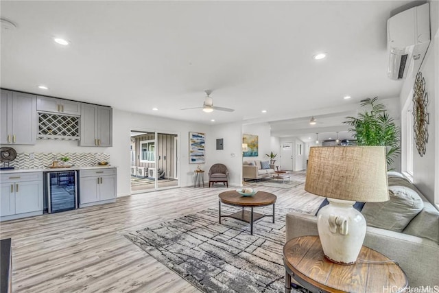 living room with ceiling fan, a wall mounted AC, bar area, light wood-type flooring, and wine cooler