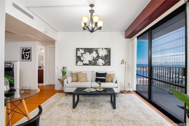 living area featuring a textured ceiling, a chandelier, a water view, wood finished floors, and visible vents