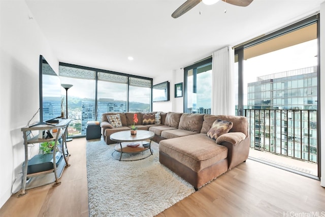 living area featuring light wood-style floors, ceiling fan, and a wall of windows