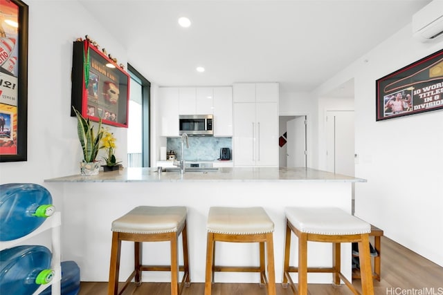 kitchen with white cabinets, light countertops, a wall mounted AC, stainless steel microwave, and modern cabinets