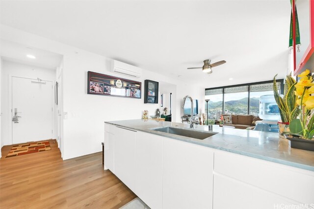 kitchen featuring a sink, white cabinetry, open floor plan, an AC wall unit, and light wood finished floors