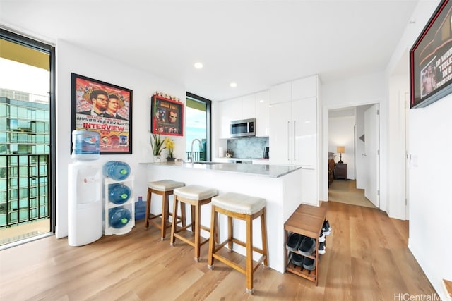 kitchen with a peninsula, a breakfast bar, white cabinetry, backsplash, and stainless steel microwave