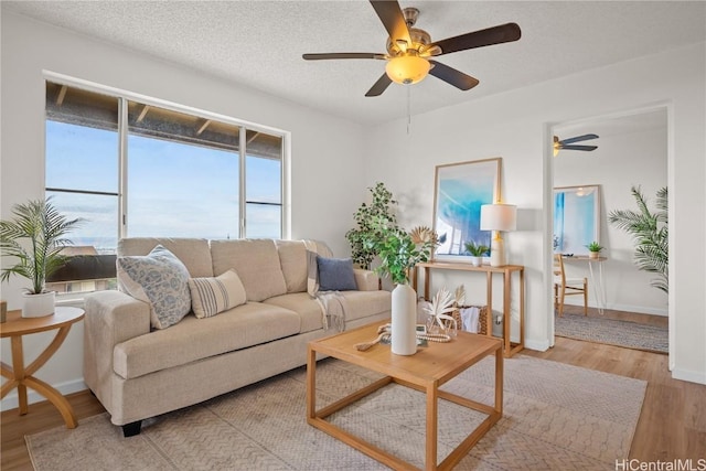 living room with ceiling fan, a textured ceiling, and light wood-type flooring