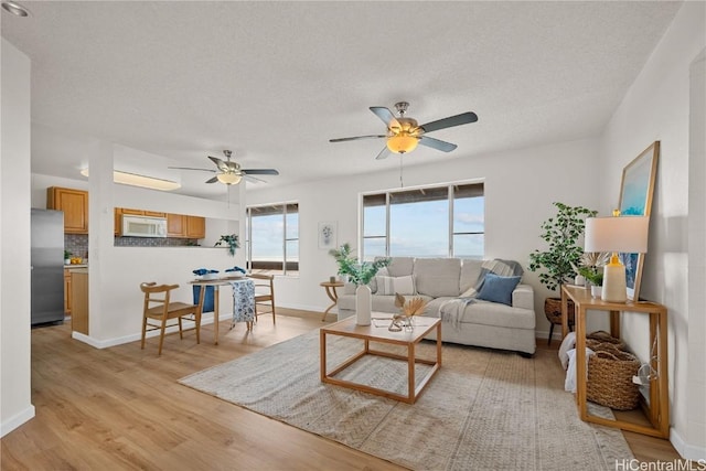 living room with ceiling fan, a textured ceiling, and light hardwood / wood-style floors