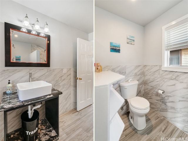 bathroom featuring a wainscoted wall, a sink, tile walls, and toilet