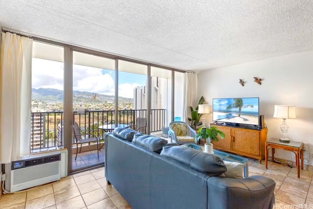 living area with a wall mounted air conditioner, expansive windows, light tile patterned flooring, a mountain view, and a textured ceiling