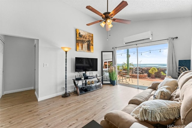 living room with a textured ceiling, ceiling fan, high vaulted ceiling, a wall mounted air conditioner, and light wood-type flooring