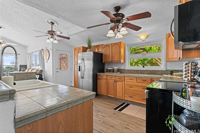 kitchen featuring tile countertops, stainless steel appliances, lofted ceiling, sink, and light wood-type flooring