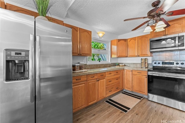 kitchen with appliances with stainless steel finishes, a textured ceiling, decorative backsplash, ceiling fan, and light wood-type flooring