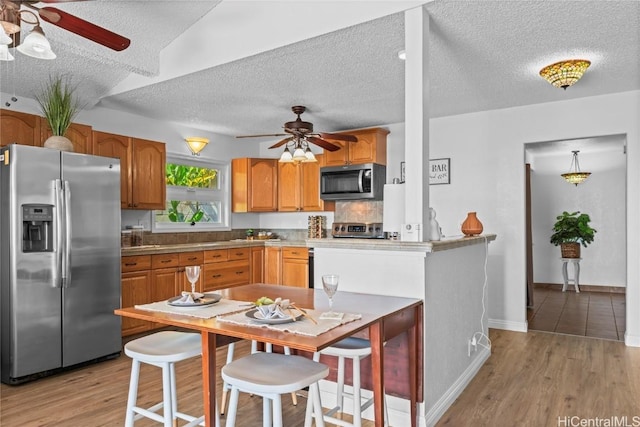 kitchen with ceiling fan, light hardwood / wood-style flooring, stainless steel appliances, and a textured ceiling