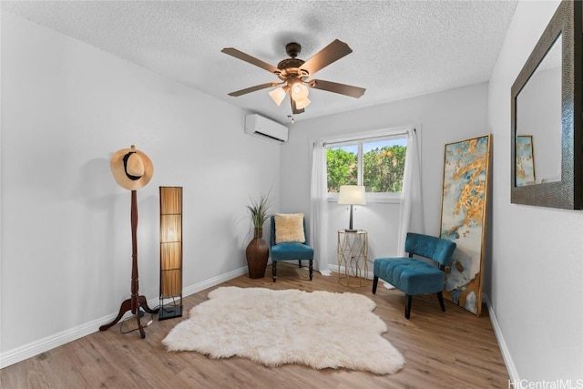 sitting room featuring an AC wall unit, a textured ceiling, and light hardwood / wood-style flooring