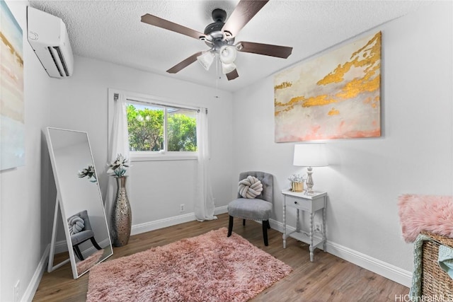 sitting room featuring an AC wall unit, a textured ceiling, ceiling fan, and hardwood / wood-style floors