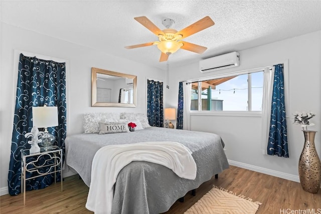 bedroom featuring hardwood / wood-style floors, a textured ceiling, ceiling fan, and a wall unit AC