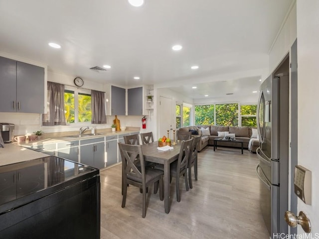 kitchen with gray cabinets, a wealth of natural light, stainless steel fridge, and light hardwood / wood-style flooring