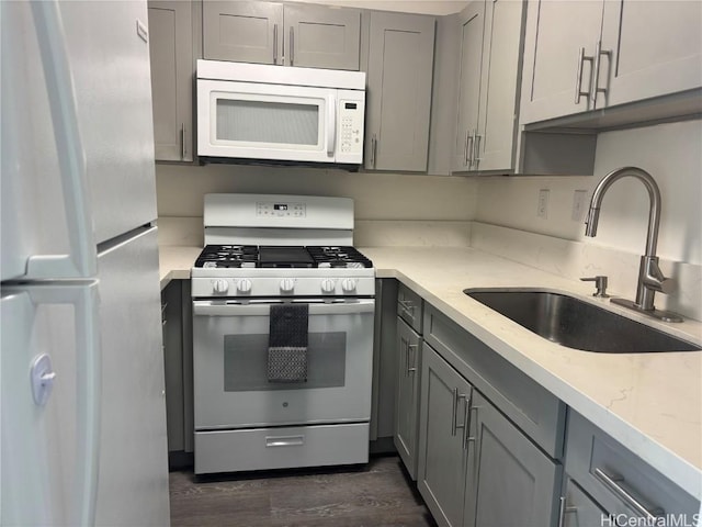 kitchen featuring light stone countertops, white appliances, gray cabinets, and a sink