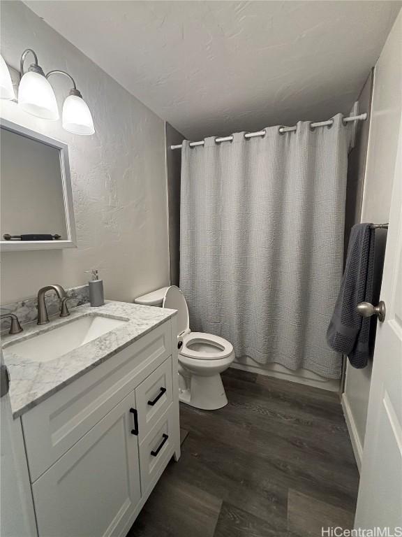 full bathroom with shower / tub combo with curtain, a textured wall, toilet, vanity, and wood finished floors