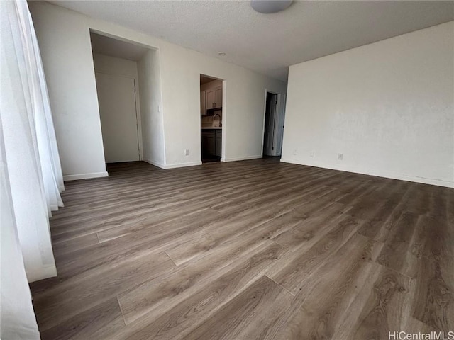 empty room featuring a textured ceiling, wood finished floors, and baseboards