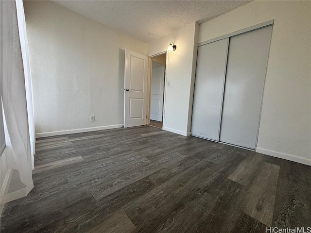 unfurnished bedroom featuring a closet, a textured ceiling, baseboards, and dark wood-style flooring