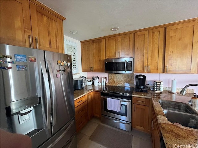 kitchen with appliances with stainless steel finishes, brown cabinets, a sink, and light tile patterned floors