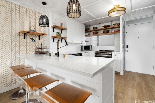 kitchen featuring open shelves, stainless steel appliances, white cabinets, a peninsula, and a kitchen bar