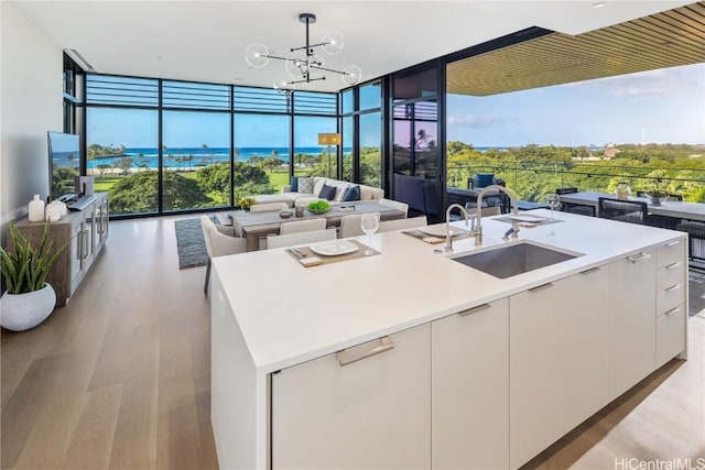 kitchen with sink, a center island with sink, white cabinets, and decorative light fixtures