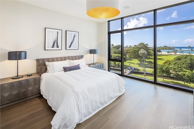 bedroom with hardwood / wood-style flooring, a water view, and a wall of windows