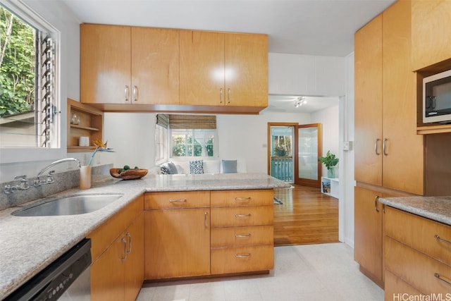 kitchen featuring stainless steel appliances, a peninsula, a sink, light stone countertops, and light floors