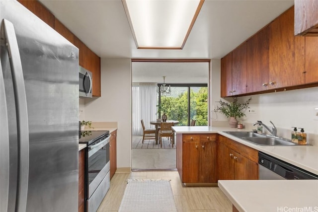 kitchen featuring a peninsula, a sink, light countertops, appliances with stainless steel finishes, and brown cabinets