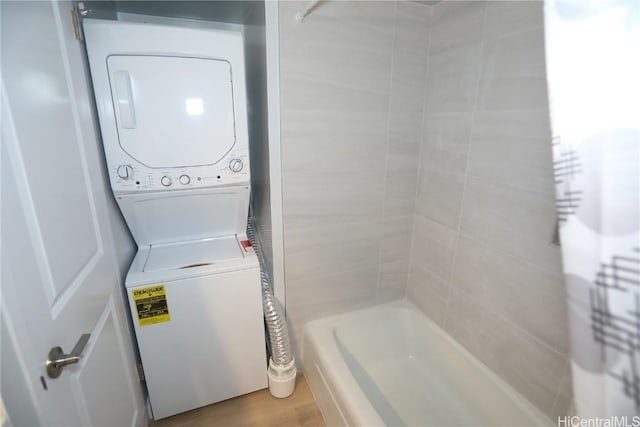 clothes washing area with stacked washing maching and dryer, radiator heating unit, laundry area, and wood finished floors