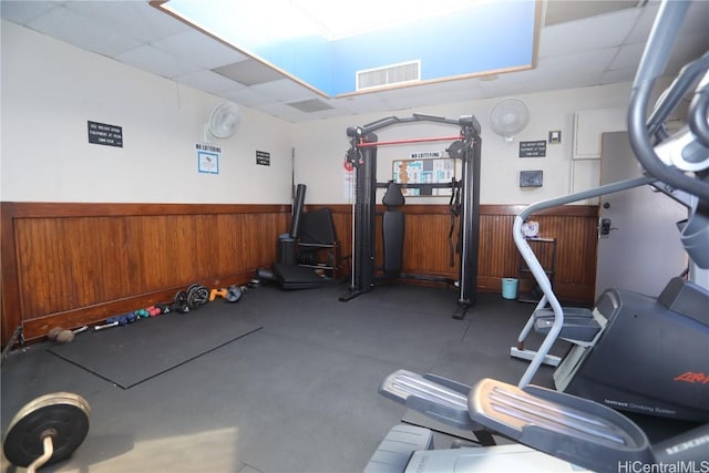 exercise room with a paneled ceiling, wood walls, and wainscoting