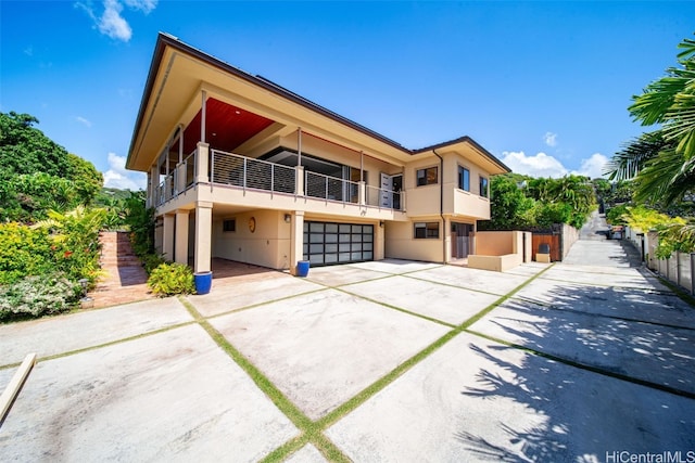 view of front facade with fence, concrete driveway, stucco siding, a balcony, and a garage