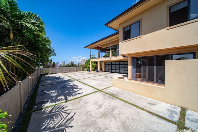 view of patio featuring a balcony, an attached garage, fence, and driveway