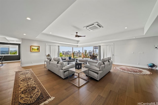 living room with a view of city, a tray ceiling, wood finished floors, recessed lighting, and baseboards