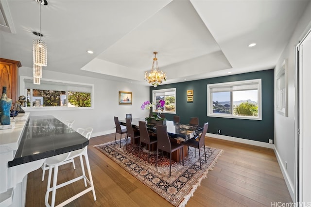 dining room featuring hardwood / wood-style floors, a raised ceiling, baseboards, and an inviting chandelier